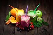 High angle view of three blended fruit smoothies in glass jars surrounded by colorful fresh fruits on dark wood table. DSRL studio photo taken with Canon EOS 5D Mk II and Canon EF 100mm f/2.8L Macro IS USM